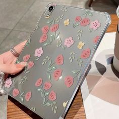 a person holding an ipad case with pink flowers on it and a coffee cup in the background