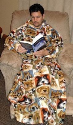 a man sitting in a chair with a dog print robe on, reading a book