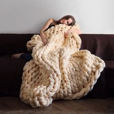 a woman is laying on a couch wrapped in a chunky blanket