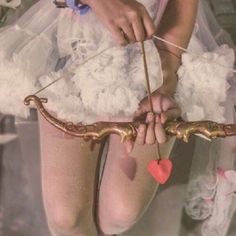 a woman in white dress holding a bow and arrow with red heart attached to it