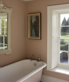 a bath tub sitting next to a window in a bathroom under a framed painting on the wall