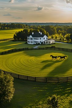 two horses running in the middle of a green field with a large white house behind it