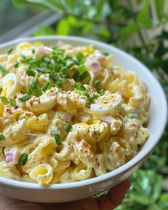 a white bowl filled with macaroni salad on top of a wooden table next to green leaves