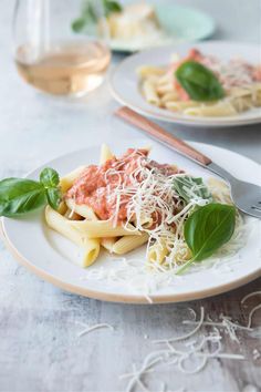 pasta with sauce, cheese and spinach on a white plate next to a glass of wine