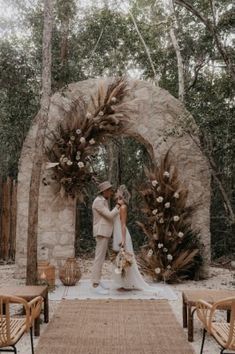 a bride and groom standing in front of a stone arch with flowers on it at their wedding ceremony