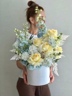 a woman holding a white vase with yellow and blue flowers