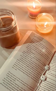 an open book sitting on top of a table next to two candles and a jar