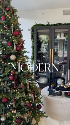 a decorated christmas tree with red and gold ornaments in front of a glass door that reads no modern