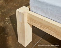 a wooden bed frame sitting on top of a floor next to a blue sheet covered pillow