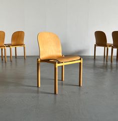 four wooden chairs are lined up in a room with white walls and concrete flooring