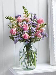 a vase filled with pink and purple flowers on top of a white shelf next to a window