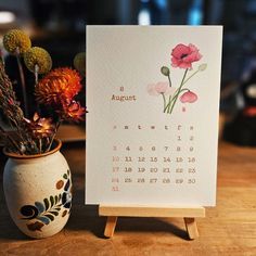 a calendar sitting next to a vase with flowers in it on top of a table