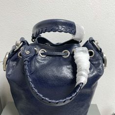 Balenciaga 's popular 'Le Cagole' series is a modern interpretation of its 'City' handbags - reshaped into a bucket bag design to inject a new soul into it. The large size adds two round top handles, combining classic and Modern trends are perfectly integrated. On the basis of retaining the original DNA of the motorcycle bag's flat rivets, delicate buckles and tassel zippers, it adds adjustable woven shoulder straps and a cute and playful heart-shaped mirror, which perfectly softens the neutral New Soul, Shaped Mirror, Dumpling Bag, Motorcycle Bag, Lv Purse, Lv Shoes, Gucci Bamboo, Lv Handbags, Orange Bag