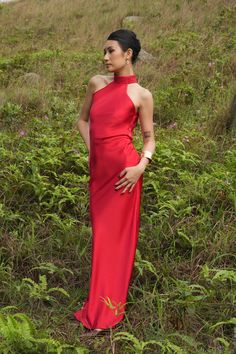 a woman in a long red dress standing on the side of a hill with her hands on her hips