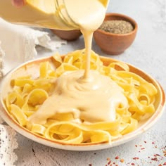 a person pouring sauce on top of a plate of pasta in a bowl with other ingredients