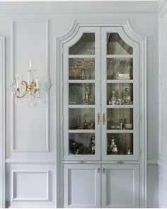 a white china cabinet with glass doors and chandelier