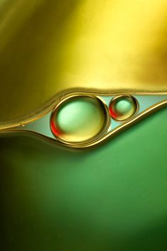 two drops of water sitting on top of green and gold material with red dots in the middle