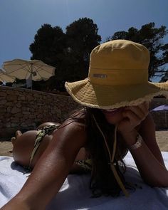 a woman laying on top of a towel wearing a yellow hat