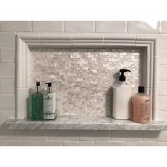 a white shelf with two bottles and soaps on it in front of a tiled wall