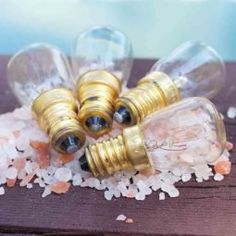 three clear glass bottles with gold caps sitting on top of some white rocks and gravel