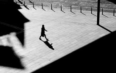 a person walking down a sidewalk with an umbrella in their hand and shadows on the ground