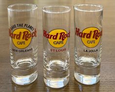 three shot glasses sitting on top of a wooden table next to each other with the words hard rock cafe