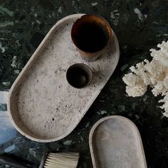 a cup and brush are sitting on a marble tray next to some white flowers in the background