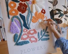 a woman is painting flowers on a canvas with crocheted yarns and scissors