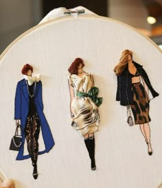 three hand embroidered pictures of women in dresses and purses on a white wall hanging