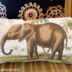 an elephant pillow sitting on top of a bed next to a black headboard with decorative wallpaper