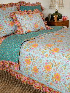 the bed is made with colorful flowers and ruffled bedspread, along with matching pillows