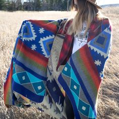 a woman standing in a field wearing a colorful blanket