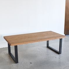 a wooden table sitting on top of a cement floor next to a white wall with black metal legs