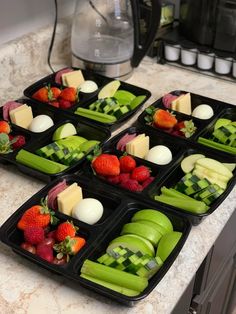 four trays filled with assorted fruits and vegetables sitting on a counter top next to a blender