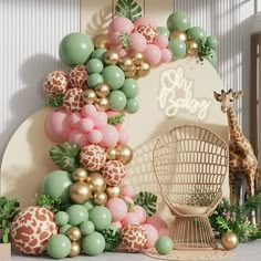 a giraffe standing next to a balloon arch with balloons and greenery on it