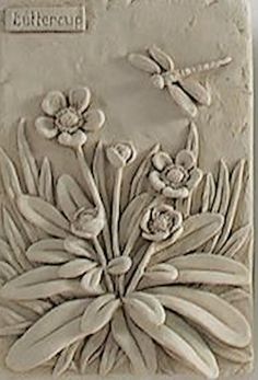 a white tile with flowers and dragonflies on the side, in front of a gray wall