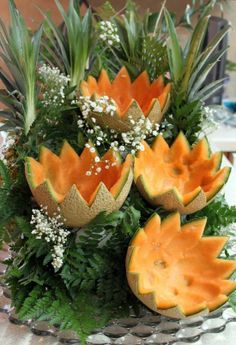 an arrangement of fruit is displayed on a table with greenery and white flowers in the center