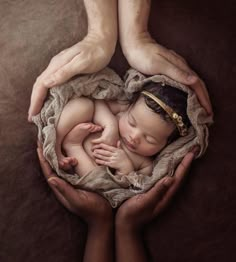 a newborn baby is curled up in the middle of two hands while being held by someone's hands