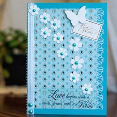 a blue card with white flowers on it sitting on a table next to a potted plant