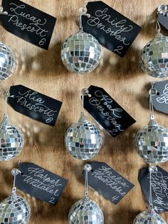 disco ball ornaments with name tags hanging from them on a wooden tablecloth covered wall