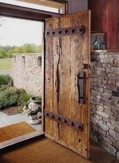 an open wooden door in front of a brick wall and stone fireplace with potted plants next to it