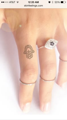 a person's hand with a small tattoo on the middle finger and an evil eye ring