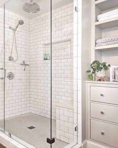 a walk in shower sitting next to a white dresser and shelves with towels on it