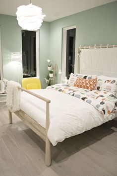 a white bed sitting in a bedroom on top of a hard wood floor next to two windows