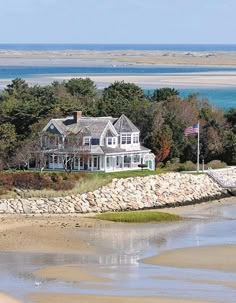 a large white house sitting on top of a sandy beach next to the ocean and trees