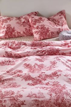 a bed covered in pink and white sheets with red toilers on the comforter