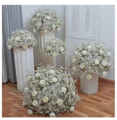 three vases filled with white flowers on top of a wooden floor