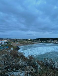 an ocean view with houses on the shore and clouds in the sky above it, at dusk