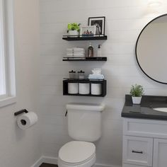 a white toilet sitting next to a bathroom sink under a round mirror on a wall