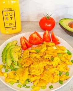 scrambled eggs, avocado and tomatoes on a plate next to an orange juice